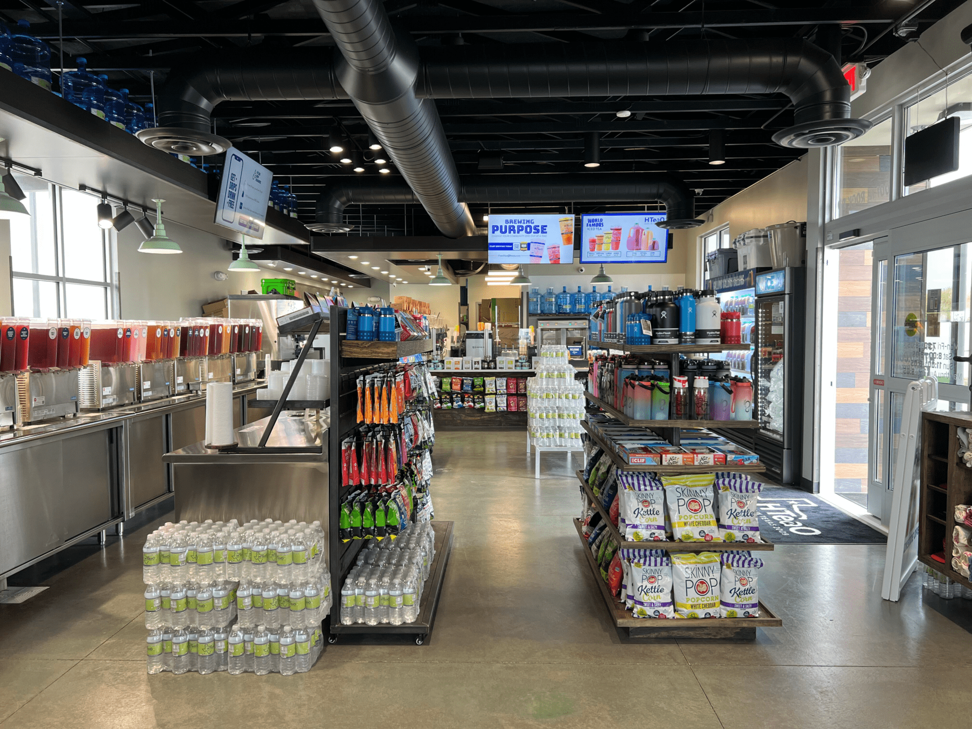 Retail store with shelves of various snacks and merchandise, and a row of containers filled with tea to the left