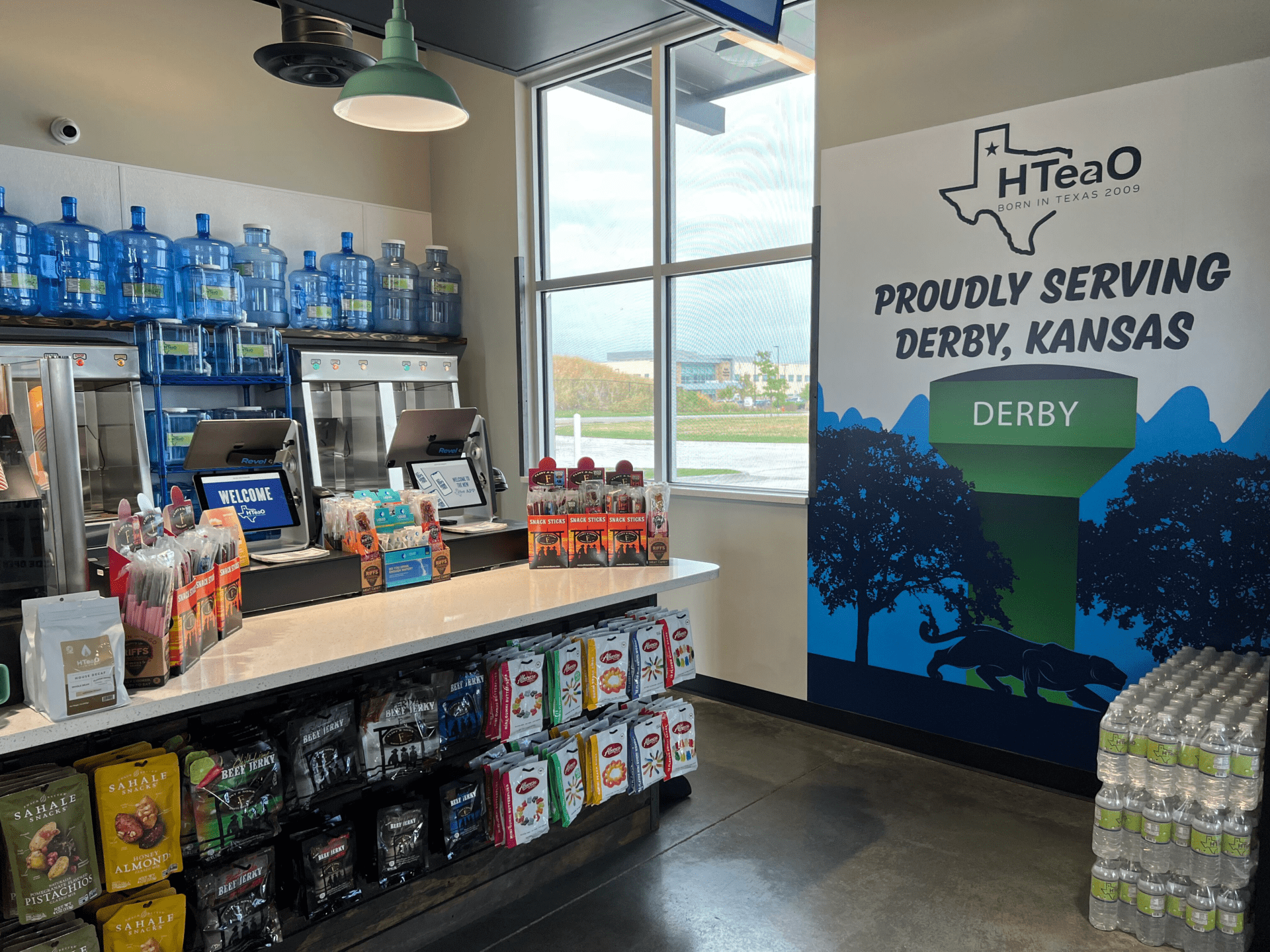 Checkout counter with snacks, a poster on the wall that says "Proudly Serving Derby, Kansas"