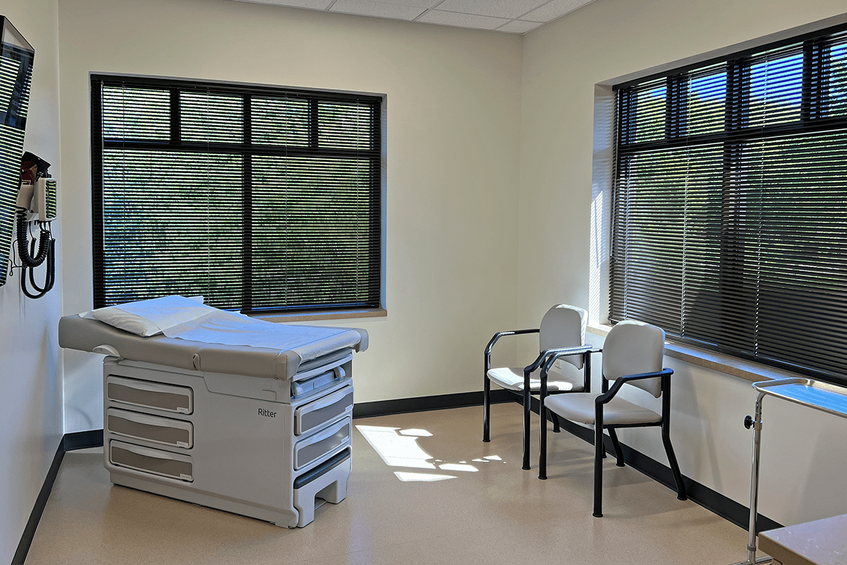 Exam room with cabinets, exam equipment, and exam table. There are large windows on two walls.