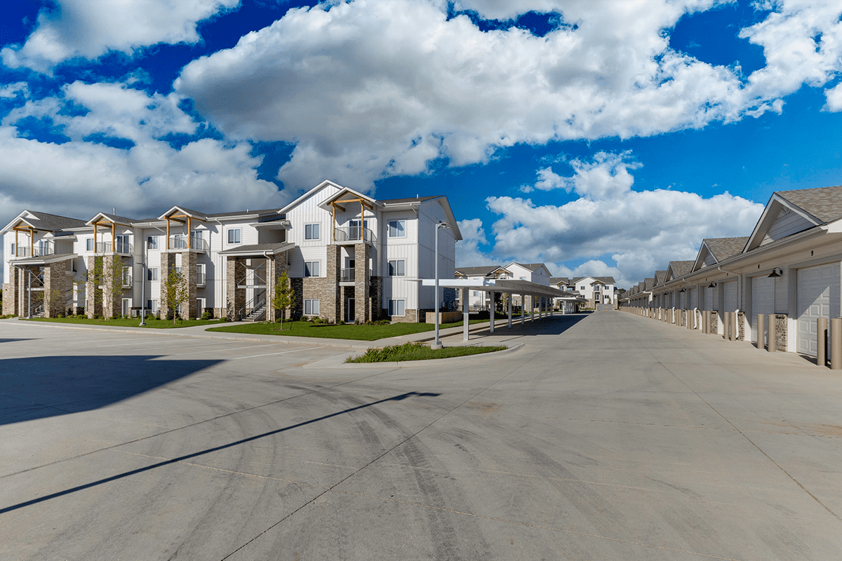 A modern apartment building with a parking lot, covered parking spaces, and garages.