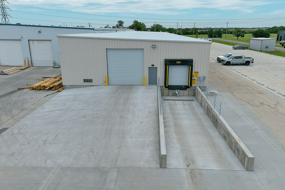 Commercial building with a white façade, multiple garage doors, and a large paved area for deliveries.