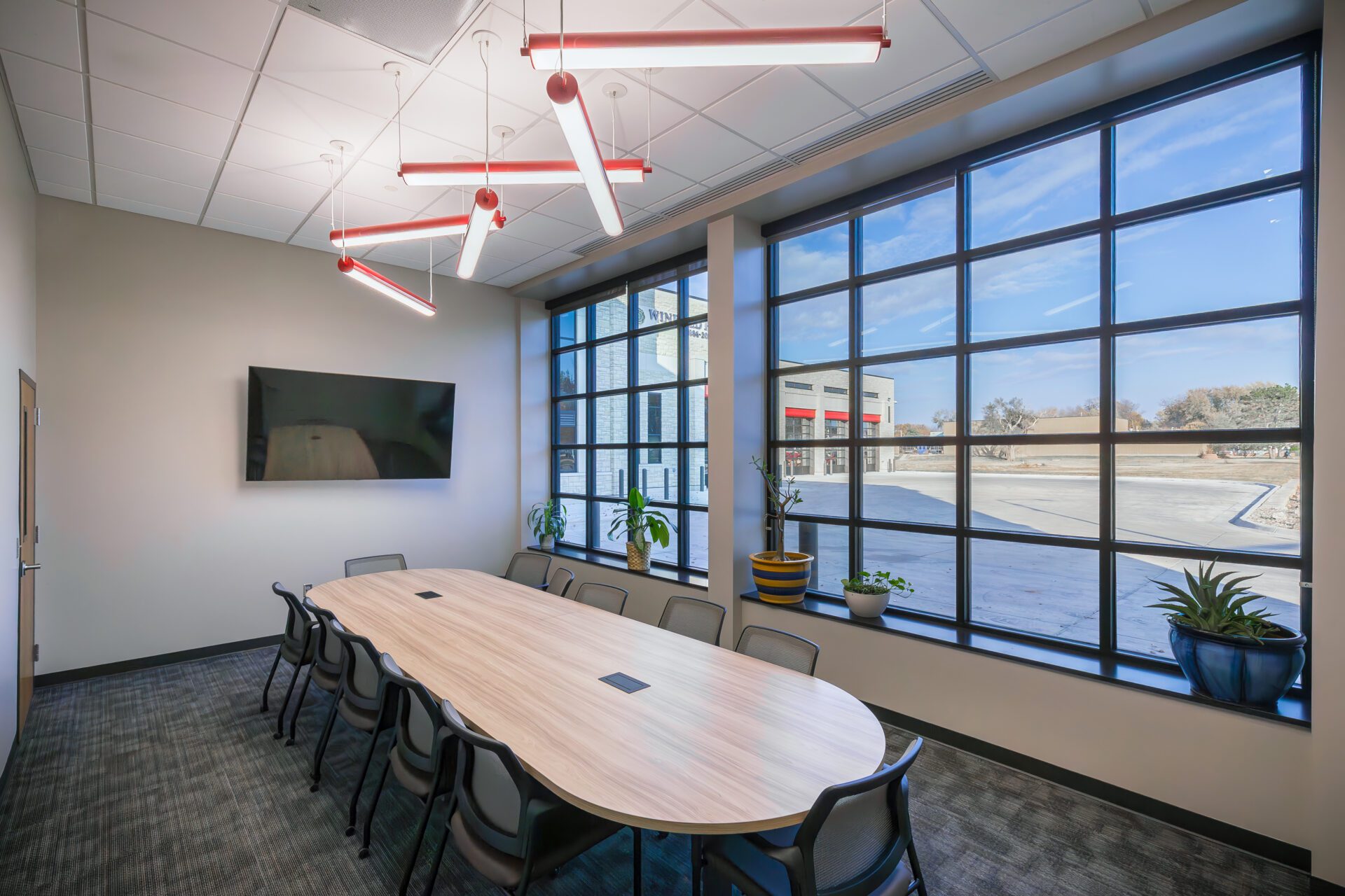 A bright and airy conference room with large windows along one wall, and cylindrical ceiling lights.